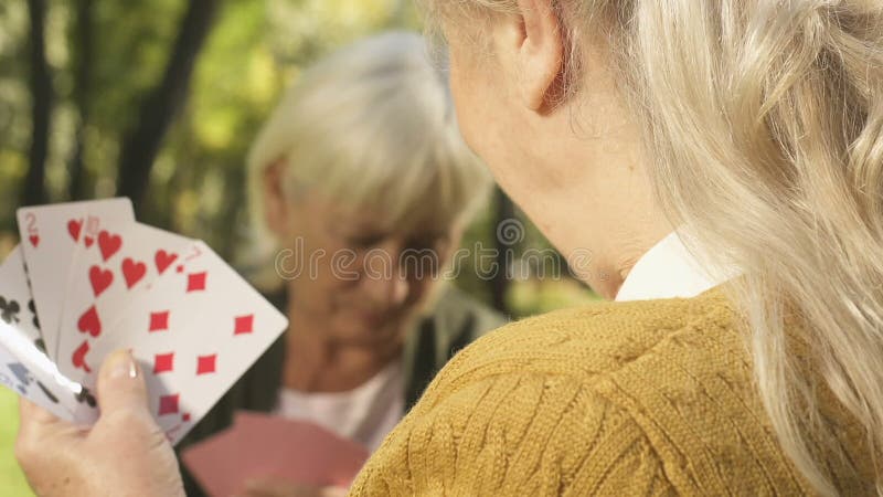 Smiling senior woman playing cards with friend outside, retirement free time