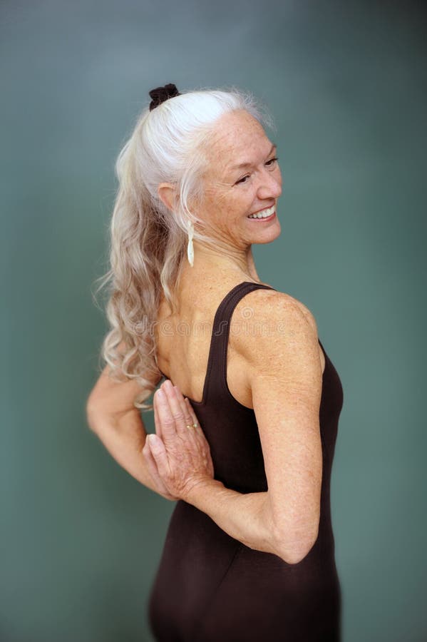 Mature woman smiling in an expressive version of the yoga mudra pose reverse prayer. Mature woman smiling in an expressive version of the yoga mudra pose reverse prayer