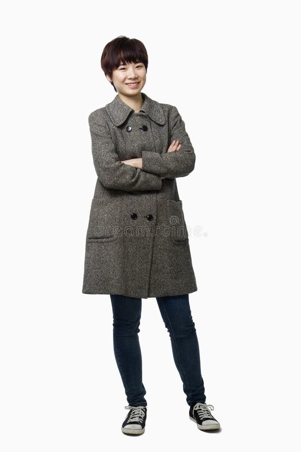 Smiling short haired young woman with arms crossed in a grey coat, studio shot, portrait