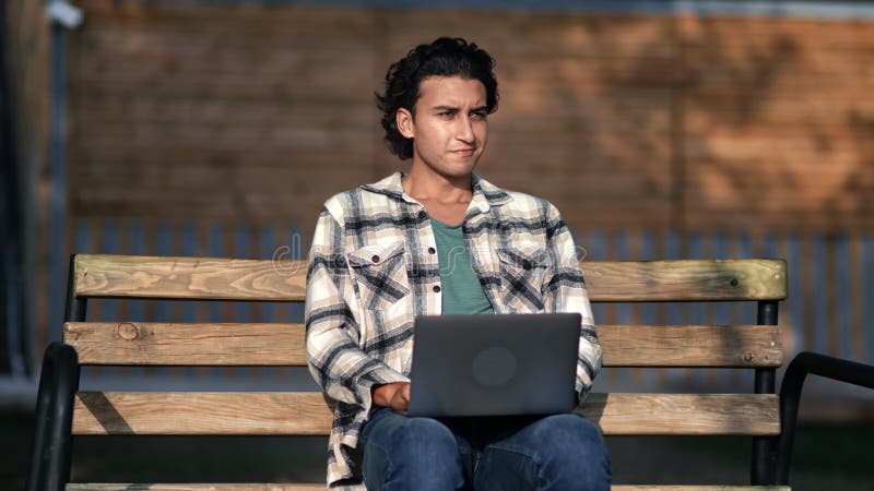 Smiling skilled Arabic male programmer developer freelancer working laptop on bench city summer park stock video