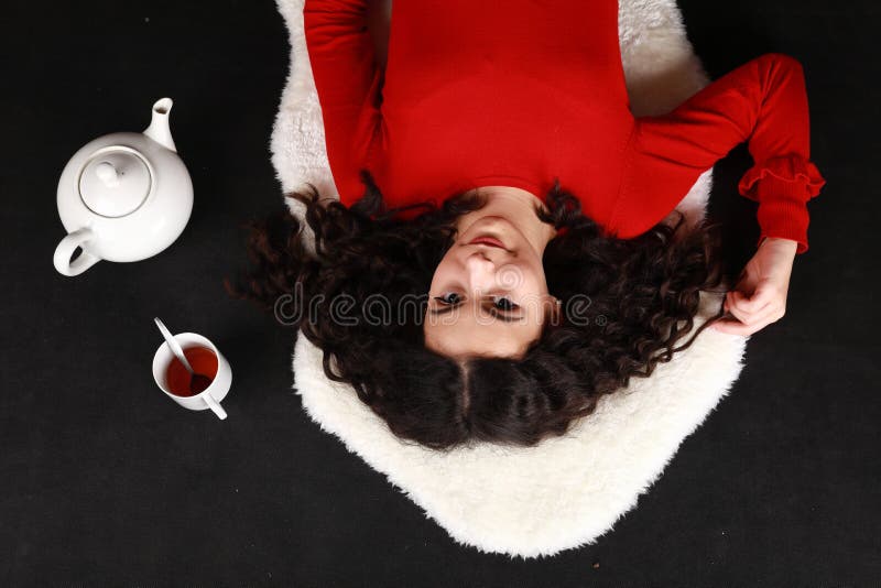 Smiling teenage girl in red blouse and black pantyhose  lying aside tea cup and teapot. Black background. Tea party concept. Smiling teenage girl in red blouse and black pantyhose  lying aside tea cup and teapot. Black background. Tea party concept.