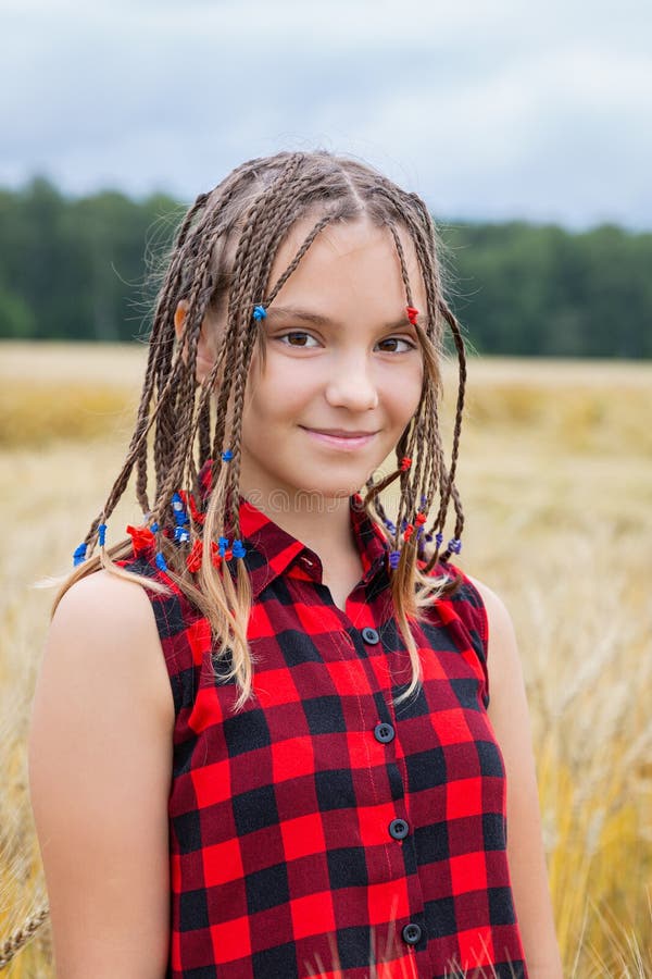 Smiling teenage girl with braids on the wind in wheat field at summer