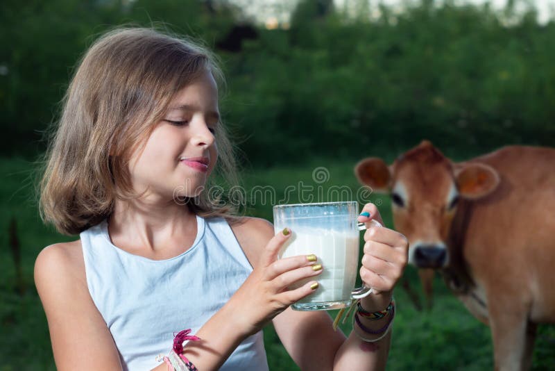 Happy Teen girl with a cup of fresh milk with a cow on the background outdoors
