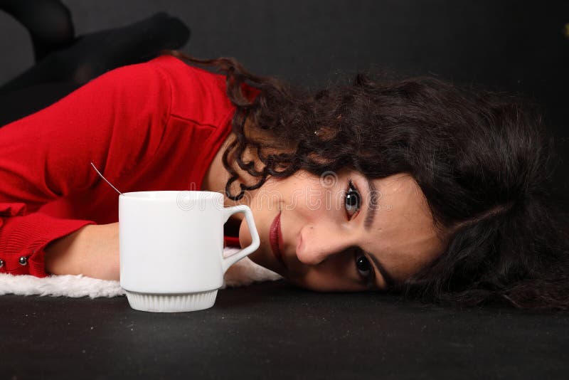 Smiling teenage girl in red blouse and black pantyhose  lying on white sheep fur. Tea cap aside of her. Black background. Tea party concept. Smiling teenage girl in red blouse and black pantyhose  lying on white sheep fur. Tea cap aside of her. Black background. Tea party concept.