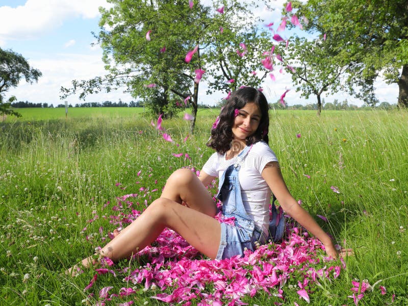 Smiling teenage girl sitting in grass under falling petals