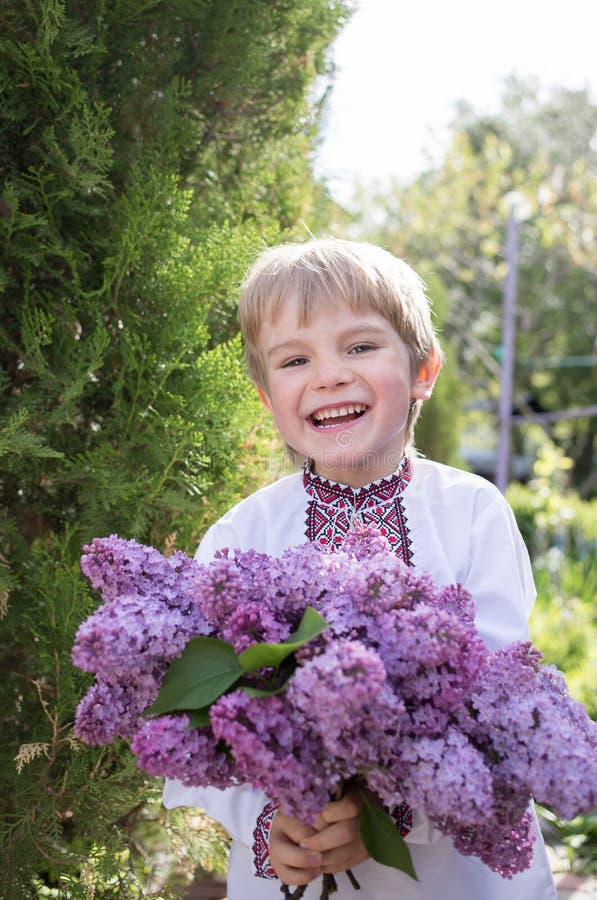 Smiling Ukrainian boy 4-5 years old in an embroidered shirt with large bouquet of lilacs. Mother`s day