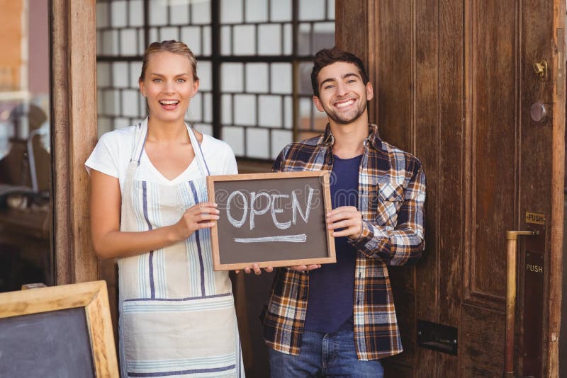 Portrait of smiling waitress and men holding chalkboard with open sign at coffee shop. Portrait of smiling waitress and men holding chalkboard with open sign at coffee shop