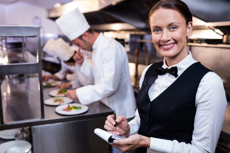 Smiling waitress with note pad in commercial kitchen