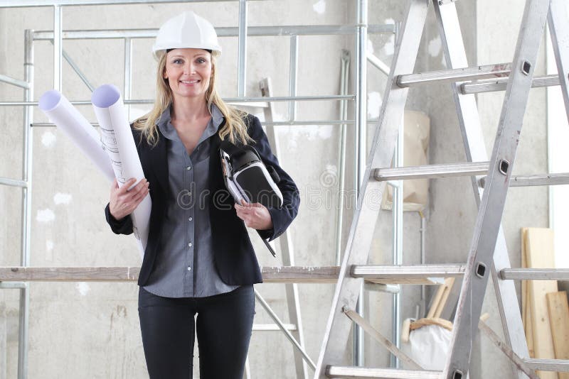 Smiling woman architect or construction engineer with virtual reality glasses wear helmet and holds blueprint inside a building stock photography