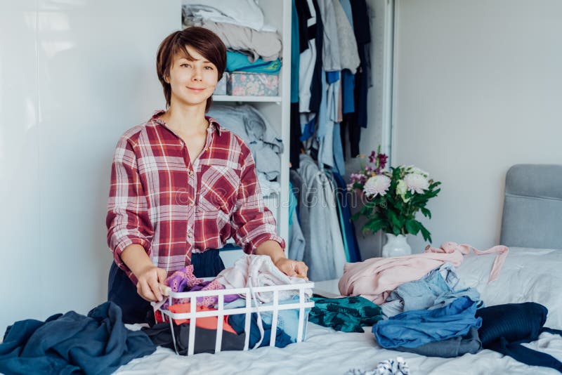 Smiling Woman with basket of selected clothes from her wardrobe for donating to a Charity. Decluttering, Sorting clothes stock photo