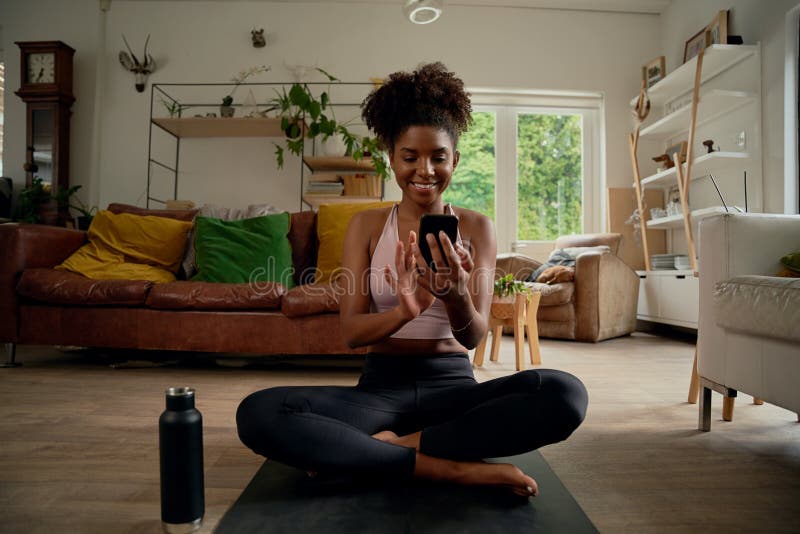 Portrait of smiling young african woman using smartphone after routine wokout with bottle besides at home royalty free stock photography