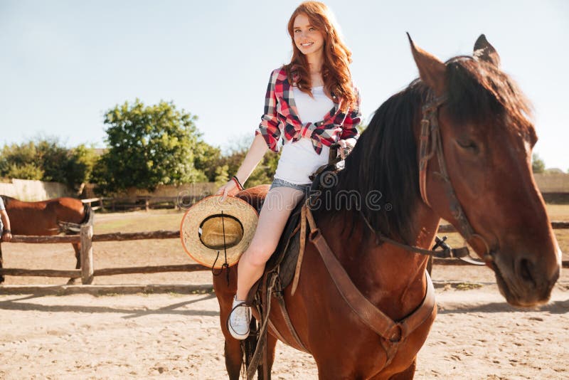 Smiling woman cowgirl riding horse in village. 