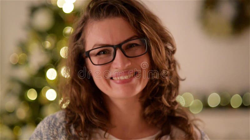 Smiling woman with curly hair and glasses on christmas tree background. Pretty girl looks at camera and smiles. Portrait