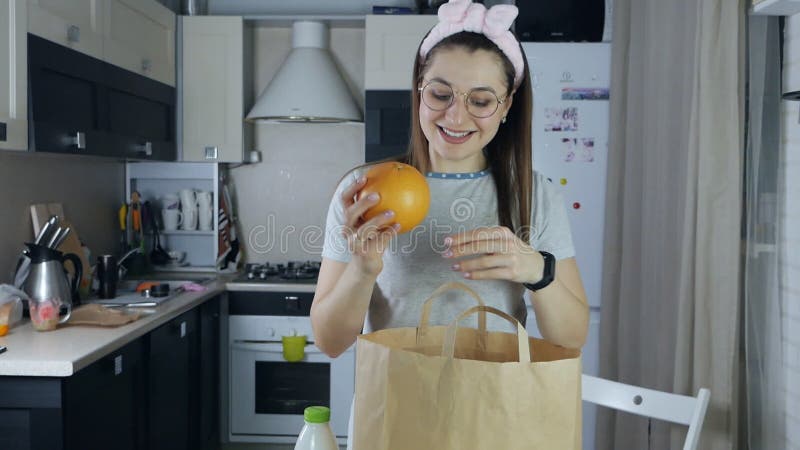 Smiling woman dismantling shopping bag and juggling fruit near paper shopping bag in kitchen. Funny positive video