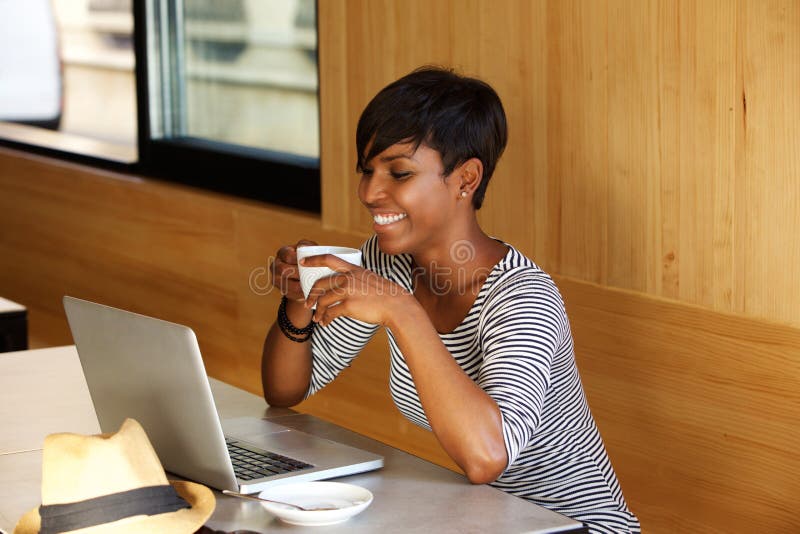 Portrait of a smiling african american woman drinking coffee and looking at laptop. Portrait of a smiling african american woman drinking coffee and looking at laptop