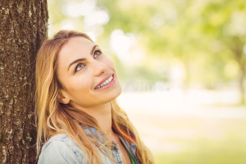 Smiling woman looking up while sitting under tree in park