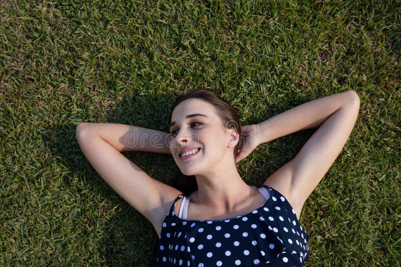 Smiling woman lying on grass with hands behind head. 