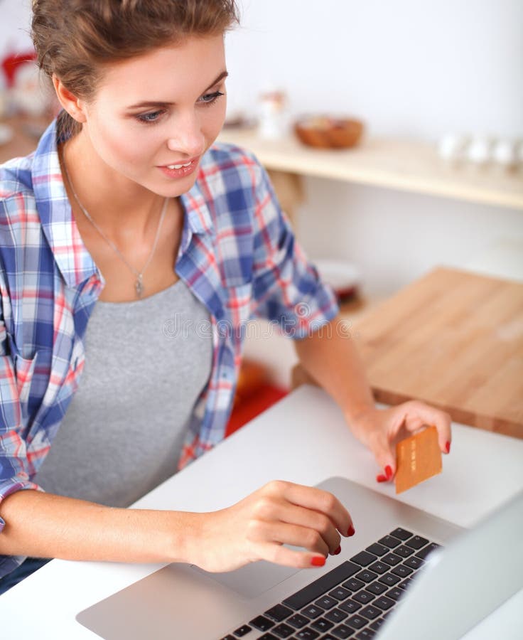 Smiling woman online shopping using computer and credit card in kitchen stock photography Smiling woman online shopping using computer and credit card in kitchen stock photography