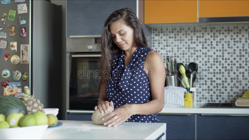 Smiling woman standing at counter with products and kneading dough in kitchen