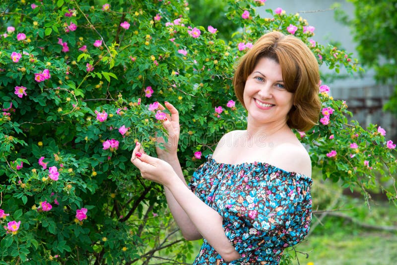 Smiling woman standing near blossoming dog rose