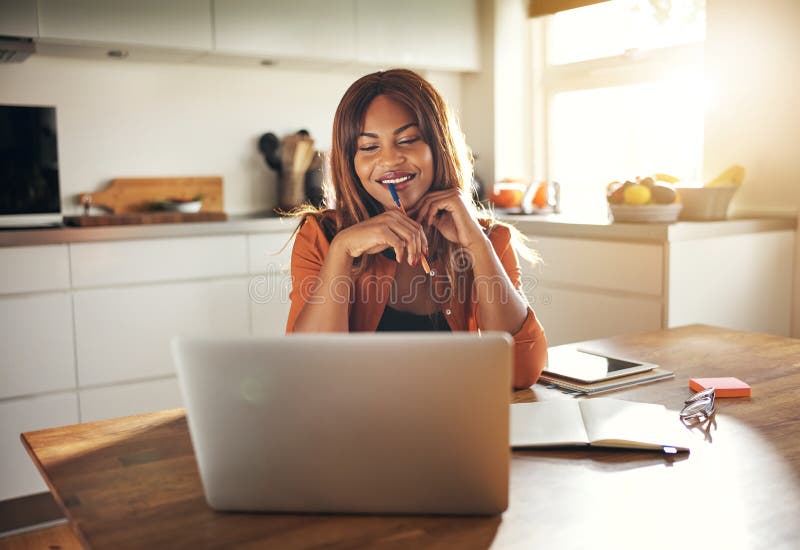 Young entrepreneur working online at her kitchen table at home stock photo Young entrepreneur working online at her kitchen table at home stock photo