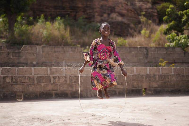 Smiling Young African Girl Warming Up With A Skipping Rope in The Backyard, candid photo of real African children in a natural village environment