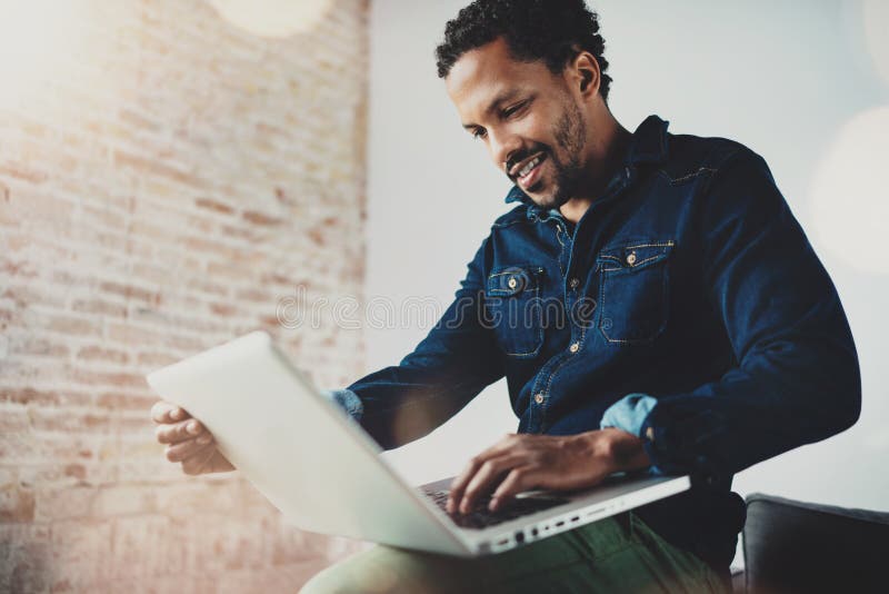 Smiling young African man using laptop while sitting at his modern coworking place.Concept of happy business people royalty free stock photography Smiling young African man using laptop while sitting at his modern coworking place.Concept of happy business people royalty free stock photography