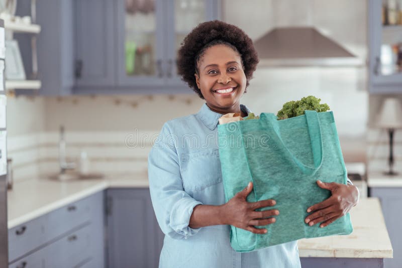 Smiling young African woman standing in her kitchen with groceries