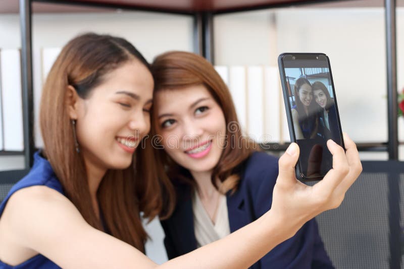 Smiling young Asian business women taking a picture or selfie together in office stock images Smiling young Asian business women taking a picture or selfie together in office stock images