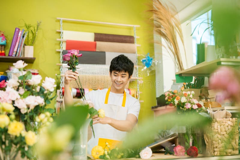 Smiling young asian florist man making bunch at flower shop