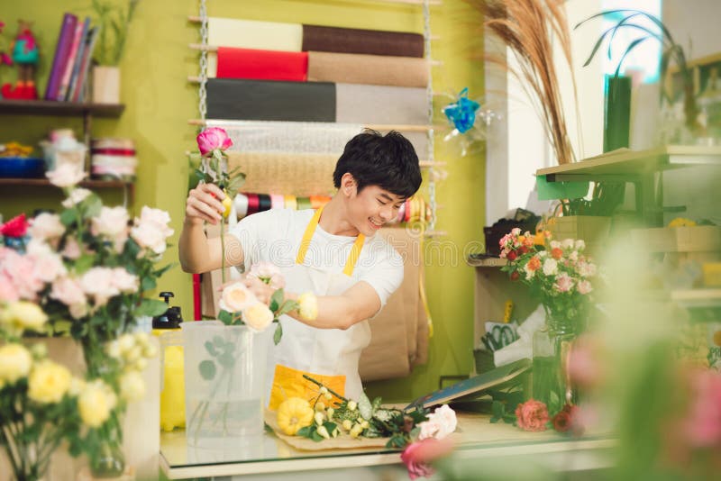 Smiling young asian florist man making bunch at flower shop