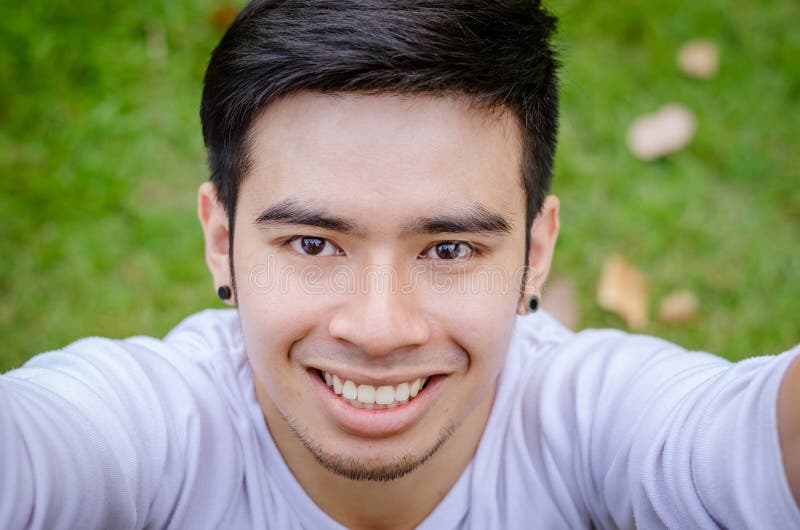 Portrait of a smiling young asian man making selfie photo in park