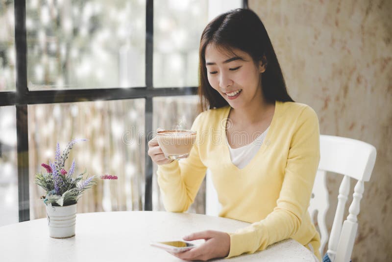 Smiling young asian woman sitting on windowsill and drinking tea at window in room. Good morning on winter day stock photography Smiling young asian woman sitting on windowsill and drinking tea at window in room. Good morning on winter day stock photography