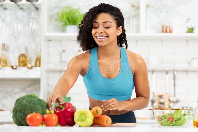 Smiling young black lady preparing vegetable salad