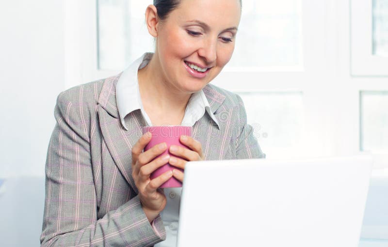 Smiling young business woman with cup using laptop