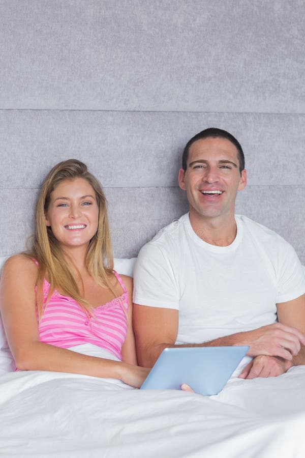 Smiling young couple using their tablet pc together in bed in bedroom at home