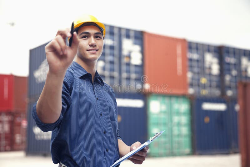 Smiling young engineer in protective work wear in a shipping yard examining cargo stock photo