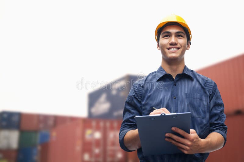 Smiling young engineer in protective work wear in a shipping yard examining cargo royalty free stock photos