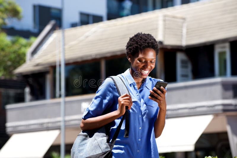 Smiling young female student walking outdoors and reading text message on smart phone stock photo Smiling young female student walking outdoors and reading text message on smart phone stock photo