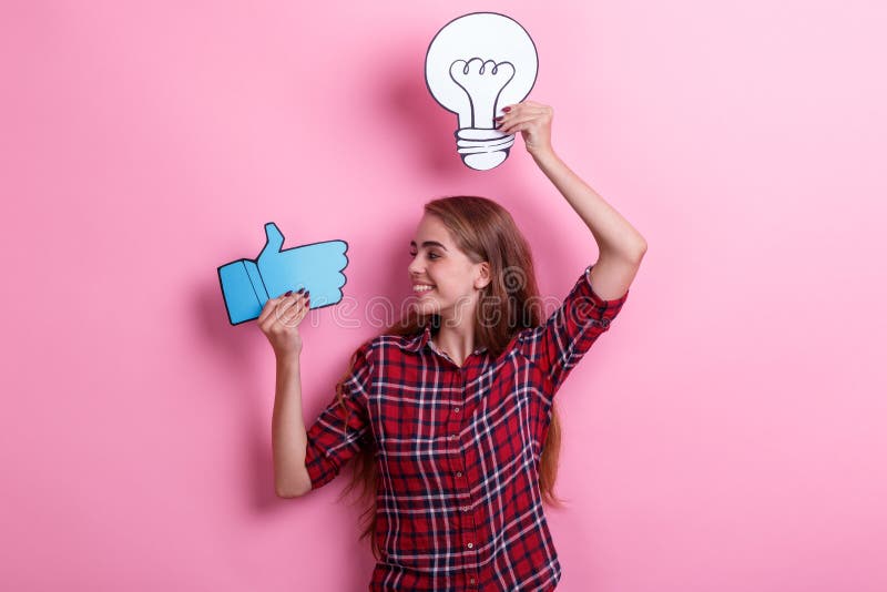 Smiling young girl holding a image of a bulb and a thumb-up sign and looking at it. Concept of the idea. stock photos Smiling young girl holding a image of a bulb and a thumb-up sign and looking at it. Concept of the idea. stock photos
