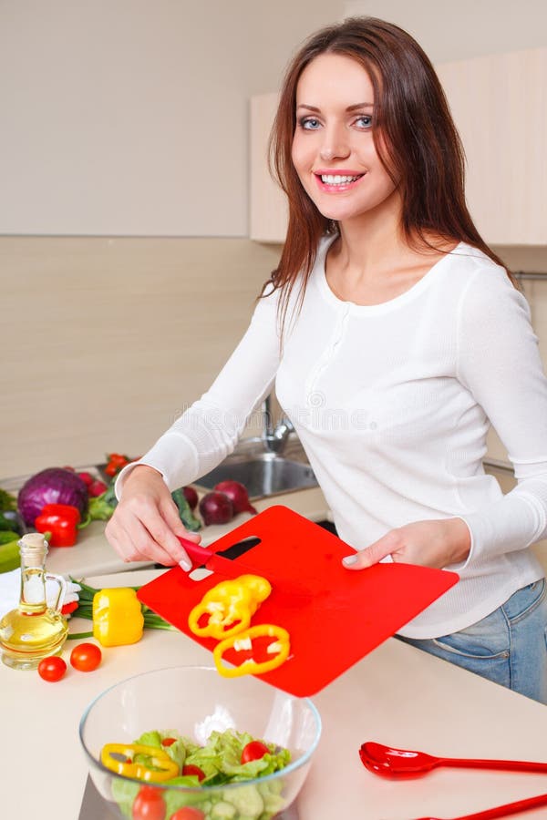 Smiling young housewife mixing fresh salad