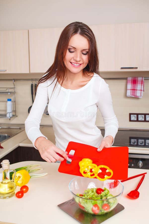 Smiling young housewife mixing fresh salad