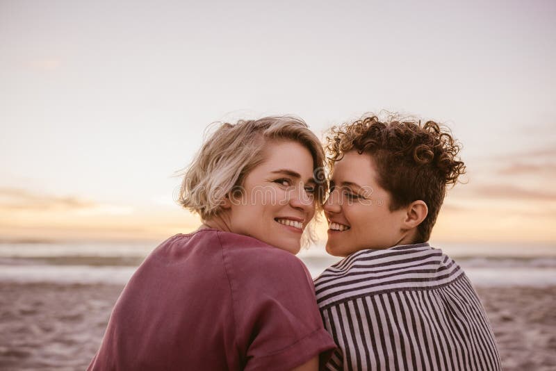 Smiling Young Lesbian Couple Watching A Beach Sunset Together Stock