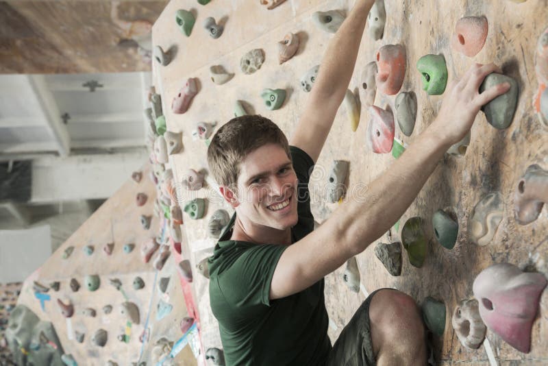 Smiling young man climbing up a climbing wall in an indoor climbing gym