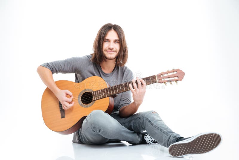 Smiling young man sitting on the floor and playing guitar