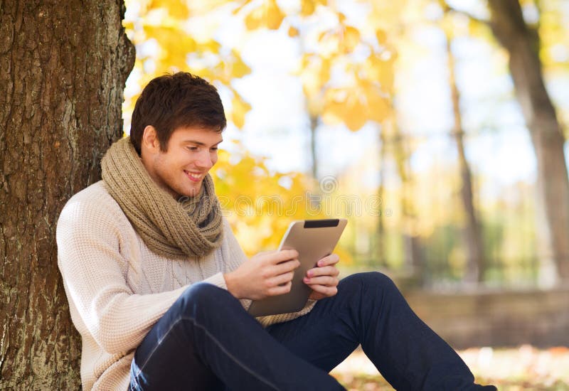 Smiling young man with tablet pc in autumn park