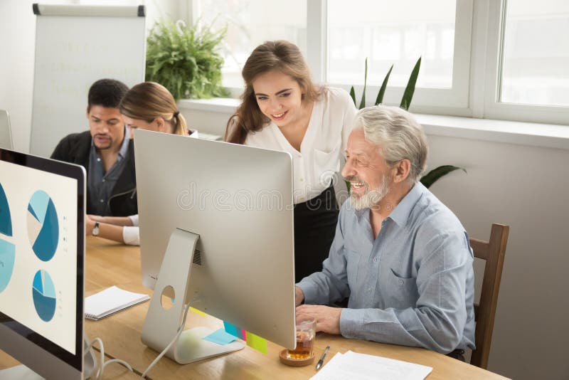 Smiling young manager helping senior worker with computer office