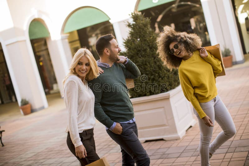 Smiling young people walking at city street and enjoying shopping together royalty free stock image