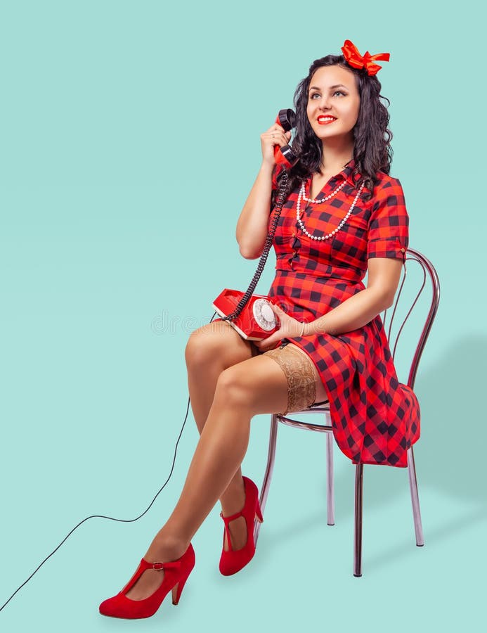 Smiling young pinup woman sitting on a chair and talking on phone