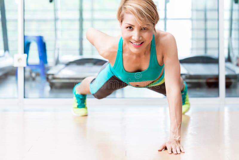 Smiling young woman doing one arm pushup in gym